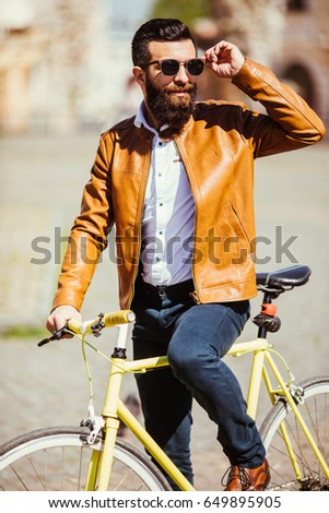 Confident young bearded man riding on his bicycle along the sunny street