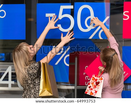 young girls carrying shopping bags looking at sale sign