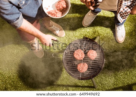Cropped shot of two young men drinking beer and grilling burgers outdoors