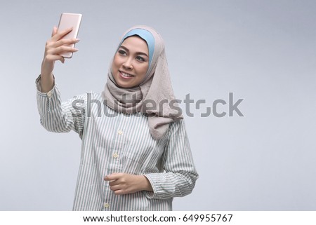 Young asian muslim woman posing talking selfie with mobile phone over dark background
