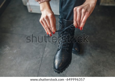 The girl in the winter in cafe. She ties laces on black leather boots. The girl has red nails.