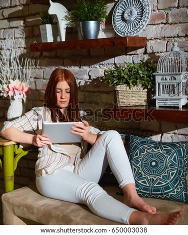 Young ginger woman relaxing at home, using tablet computer.