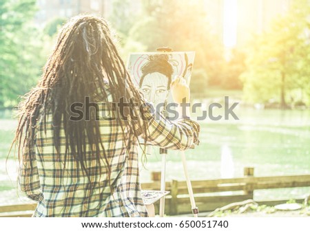 Artist girl painting self-portrait in city lake park outdoor - Young painter woman with dreadlocks at work outside at sunset - Contemporary art concept - Focus on her hand - Warm contrast filter