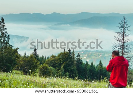 Photographer in the mountains. Guys in nature photograph forest environment, enjoying a beautiful spring afternoon. A man photographer takes pictures of the time in the mountains with a fog. 