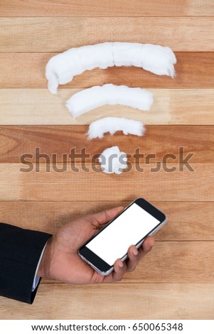 Close-up of hand holding mobile phone with wifi icon on wooden background