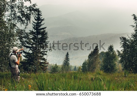 Photographer in the mountains. Guys in nature photograph forest environment, enjoying a beautiful spring afternoon. A man photographer takes pictures of the time in the mountains with a fog.