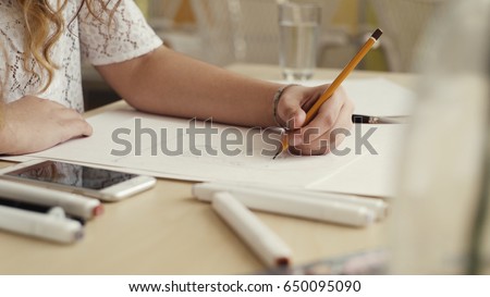 Hand of female drawing at paper in her studio. woman's hand draws a pencil. Designer clothes or tailor, animator, artist or illustrator. Royalty-Free Stock Photo #650095090