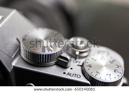 shutter speed and exposure control dial, button, on silver modern mirrorless camera