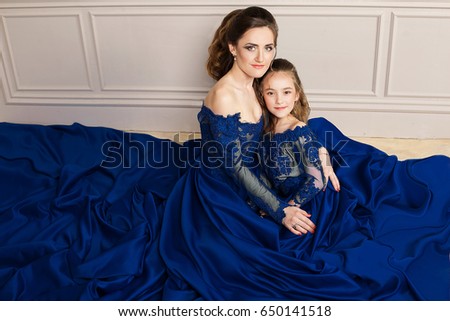 Mother and daughter hugging and looking at the camera. Happy loving family. Mother and daughter in beautiful long luxury blue dresses makeup hairstyle. Fashion family portrait. Generation relationship