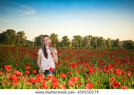 Smiling beautiful teen girl with a poppy flower posing on the poppy field at sunset. Sunny summer day