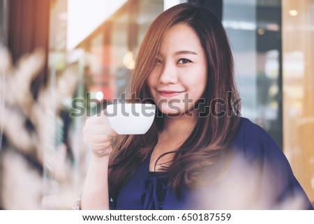 Blur image of a beautiful Asian woman smelling and drinking hot coffee with feeling good in modern cafe