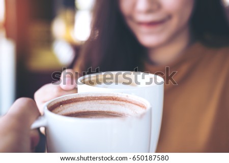 Close up image of man and woman clink coffee mugs in cafe