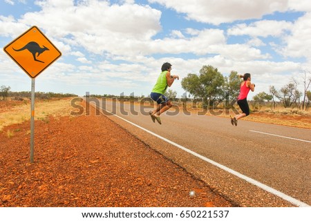 Funny couple of tourists pretend jumping like kangaroos by road sign on traditional empty highway in Northern Territory, Outback Australia. Playful sequence 2 of 2. Fun vacation concept