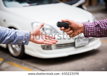 Hand giving car key on car background Royalty-Free Stock Photo #650223598
