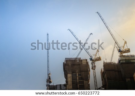 Luffing jib tower cranes on top of the high-rise building construction project. Composite precast and in-situ concrete, construction and erection concepts. Royalty-Free Stock Photo #650223772