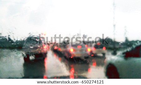 Abstract and blur background. Car waiting at red light traffic. View from front of window car though pass rain drops. 