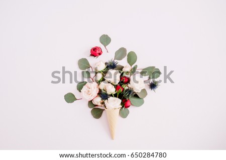 Waffle cone with red, beige roses and eucalyptus bouquet on pale pastel pink background. Flat lay, top view