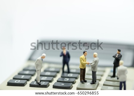 Business Concept. Two businessman miniature figures standing on calculator meeting with handshake and  another businessmen stand around the meeting. Royalty-Free Stock Photo #650296855