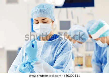 surgery, medicine and people concept - surgeon wearing medical gloves in operating room at hospital