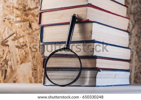 Magnifying glass and books, stacks of battered books on a wooden table. magnifier with black frame