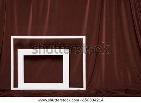 Two empty picture frames on background of brown cloth.