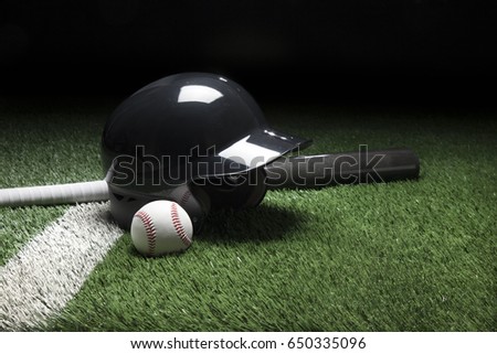 A baseball batting helmet bat and ball on a field with a white stripe and dark background