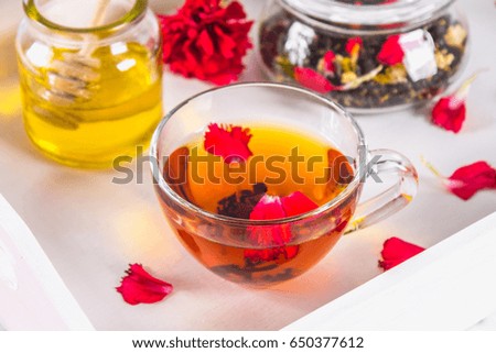 A cup of tea, a can of honey and a jar of black herbal tea on a white tray in bed