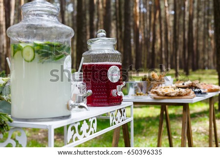 Glass jars with fresh lemonade and snacks on wooden tables. Wedding party bar in forest