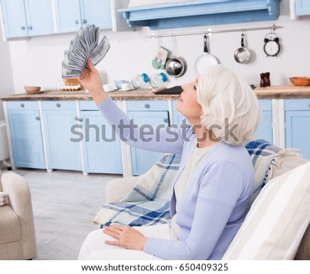 Elderly woman holding large amount of money in her hands. Elderly woman holding much money in her hands while sitting on sofa or couch.