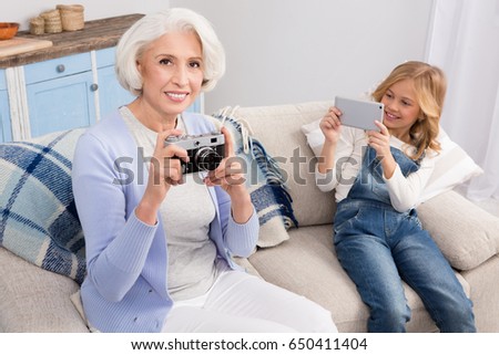 Grandmother taking pictures with film camera and girl with mobile or smart phone. Happy ladies smiling for camera.