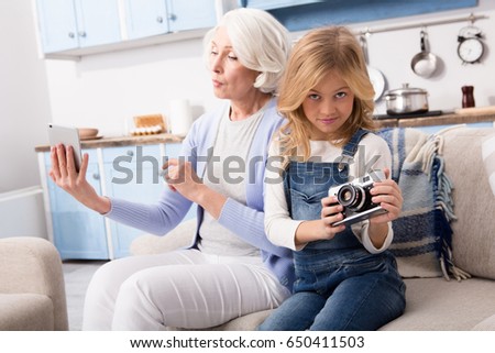 Grandmother and granddaughter studies computer gadgets of each other. Pretty ladies taking pictures on different gadgets.