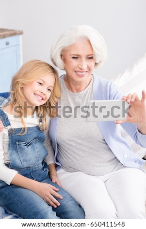 Communication with relatives through distance. Grandmother and her granddaughter looking at mobile or smart phone's camera.