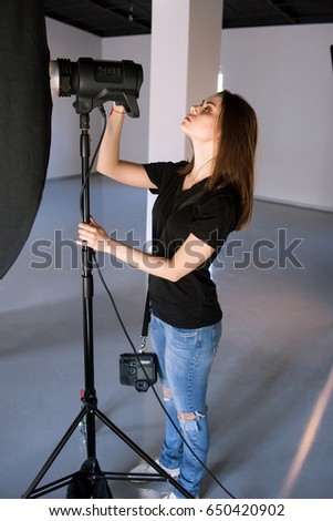 Girl photographer adjust light in studio. Beautiful woman with camera is setting photographing equipment getting ready for a photo shoot