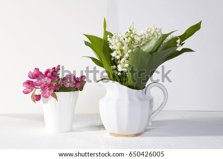Lilies of the valley in a white porcelain vase and flowers of an pink apple tree in a white cup