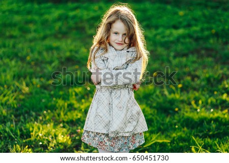 Cute blonde little girl holding her arms crossed on chest and looking at camera cunningly