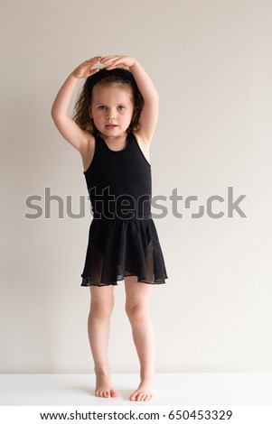 Full length view of little girl practicing ballet in black clothing against neutral background