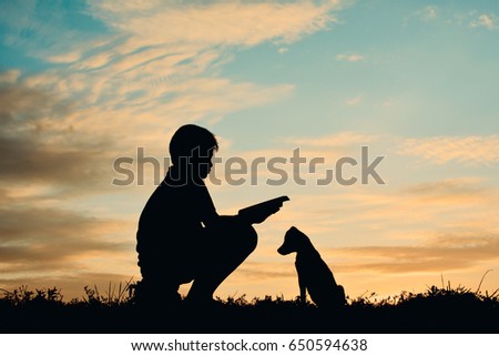 Silhouette boy reading a book with little dog on the sky sunset color of vintage tone