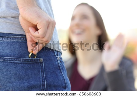 Cheater hiding wedding ring in a pocket in foreground while is dating with his lover outdoors Royalty-Free Stock Photo #650608600