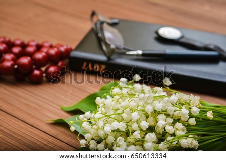A bouquet of lilies of the valley on a notebook background with a pen, a clock and glasses. Wooden background. Side view. Shallow depth of field