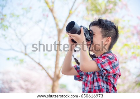 Young asian boy taking photo by camera in park