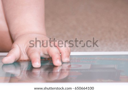 Baby boy sitting on floor playing with tablet pc. Close-up photo of the hands. Little touch pad, early learning.