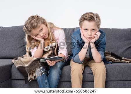 pre-adolescent bored brother and sister sitting on sofa and holding remote control Royalty-Free Stock Photo #650686249
