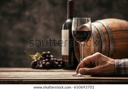 Senior wine maker tasting a glass of red wine in his cellar, wine bottle and wooden barrel on the background, wine tradition and culture concept Royalty-Free Stock Photo #650693701