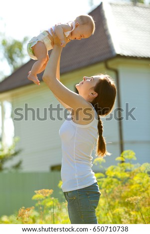 Picture of woman holding baby on arms against a house