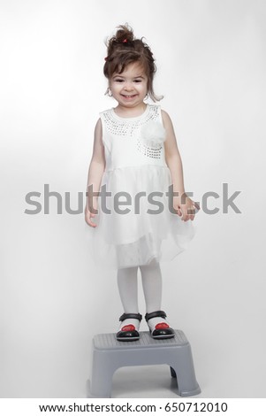  Studio portrait of a cute brunette  girl wearing fancy white dress and staying on the grey Footrest.