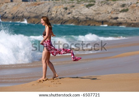 Young woman in pink sarong having fun at ocean shore
