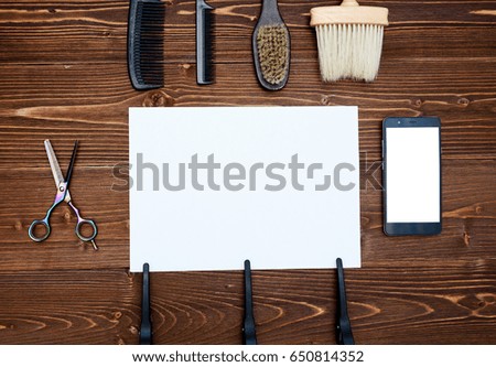 Hairdresser tools on wooden background. Blank card with barber tools flat lay. Top view on wooden table with scissors, comb and brush with empty white paper and phone, copy space