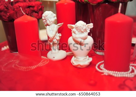 Three cupids beautiful white porcelain cute figurine with red heart and clothes pin standing on wooden background