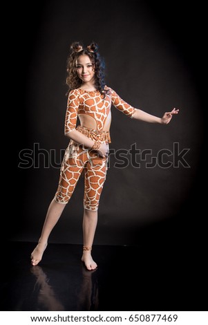 Cheerful brunette girl in orange dance suit dancing and posing on black background in studio