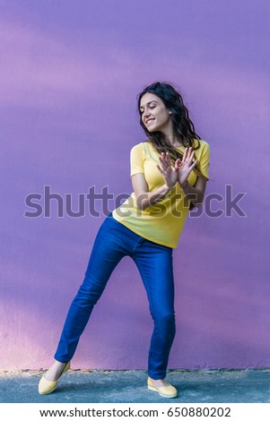 Funny young woman in yellow t-shirt on purple background